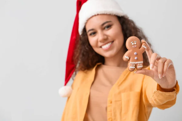 サンタの帽子の美しい若い女性とおいしいジンジャーブレッドクッキーライト背景 — ストック写真