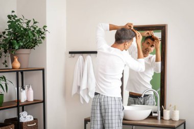 Gri saçlı stresli adam aynaya bakıyor.