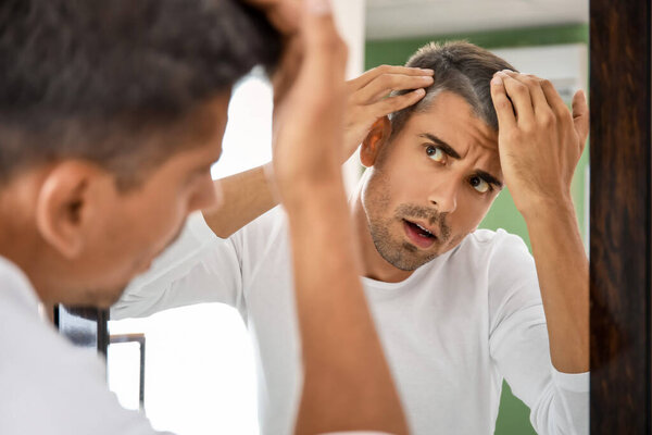 Stressed man with graying hair looking in mirror