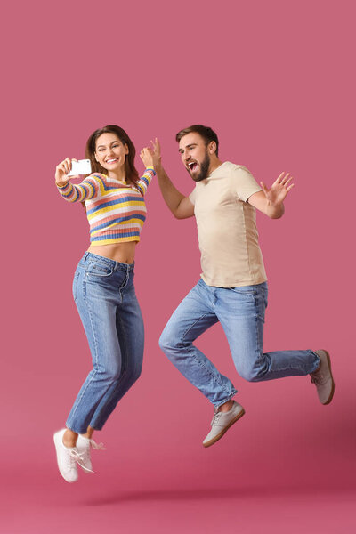 Jumping young couple taking selfie on color background