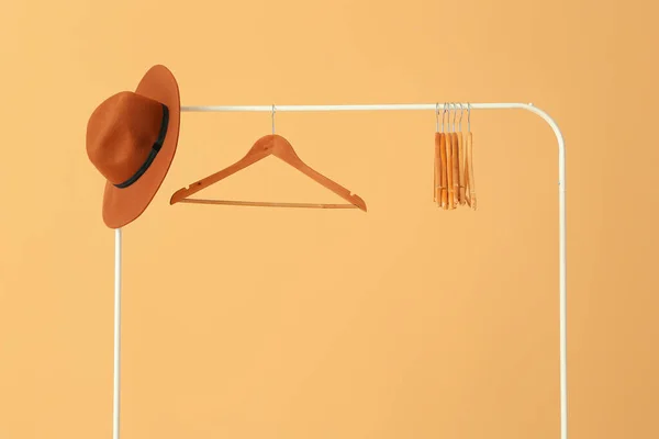 Rack with clothes hangers and hat on color background