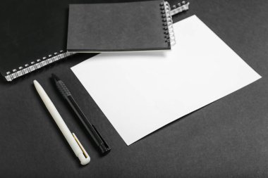 Koyu arkaplan üzerinde boş kağıt kağıtlar, defterler ve kalemlerle kompozisyon