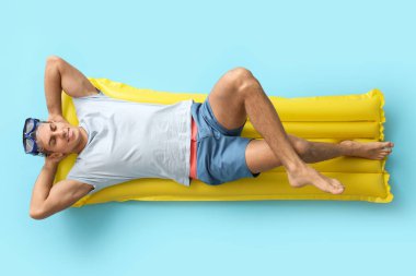 Genç adam şişme yatakta uzanmış, arka planda renkler var.