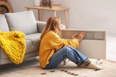 Evde elektrikli ısıtıcının yanında olgun bir kadın var. Isınma mevsimi kavramı