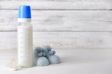 Bebek için bir şişe süt, emzik ve beyaz ahşap arka planda popolar.