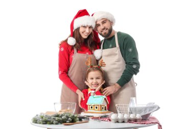 Beyaz arka planda zencefilli kurabiye evi olan mutlu bir aile. Noel kutlaması