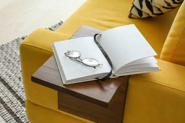 Eyeglasses and book on armrest table in room