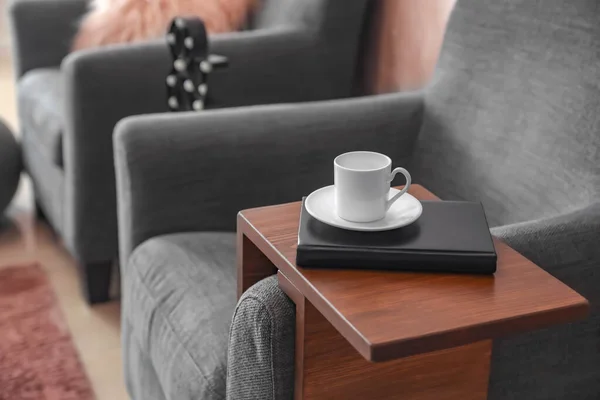 Cup of coffee and book on armrest table in room