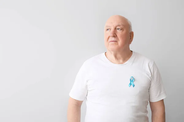 Senior man with blue ribbon on light background. Prostate cancer awareness concept