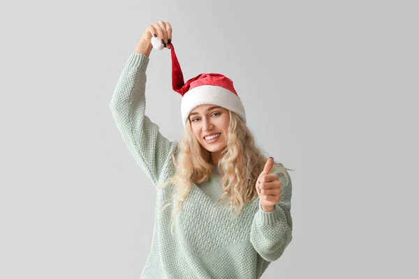戴着圣诞礼帽的年轻貌美的女人在浅色的背景上露出大拇指的姿势 — 图库照片