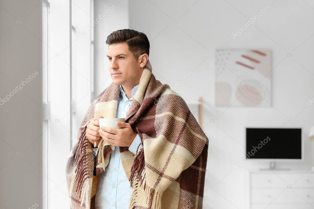 Young man with warm plaid and cup of tea at home. Concept of heating season