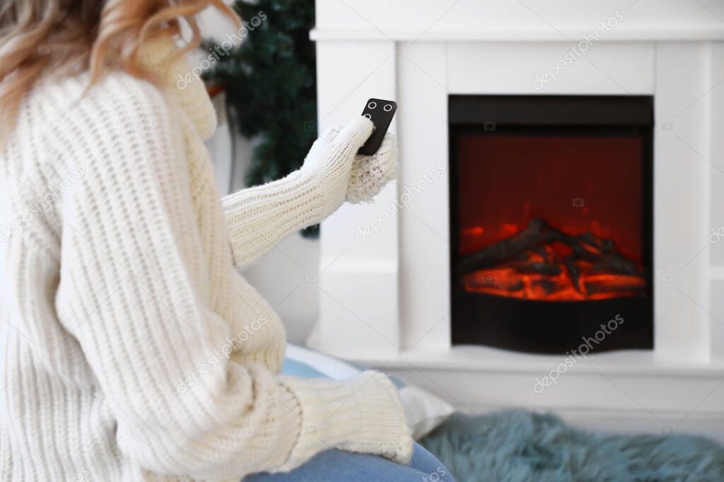 Young woman sitting near electric fireplace at home. Concept of heating season