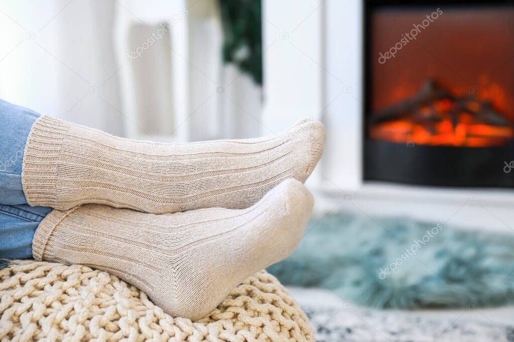 Young woman sitting near electric fireplace at home. Concept of heating season