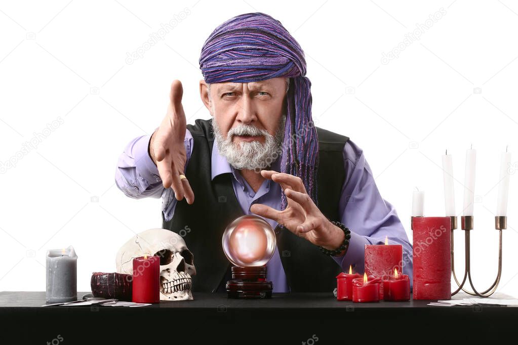 Male fortune teller with crystal ball at table on white background