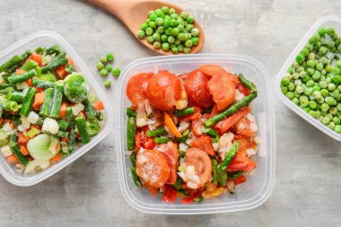 Açık arkaplanda plastik kaplarda donmuş sebzeler.