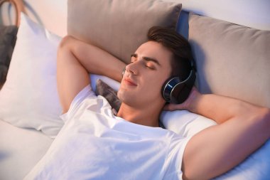 Genç adam yatak odasında müzik dinliyor.