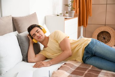 Genç adam yatak odasında müzik dinliyor.