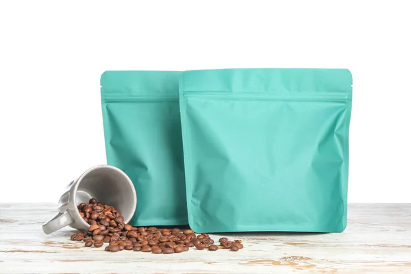 Taschen Mit Kaffeebohnen Und Tasse Auf Tisch Vor Weißem Hintergrund — Stockfoto