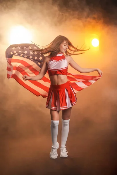 Beautiful young cheerleader with USA flag in smoke