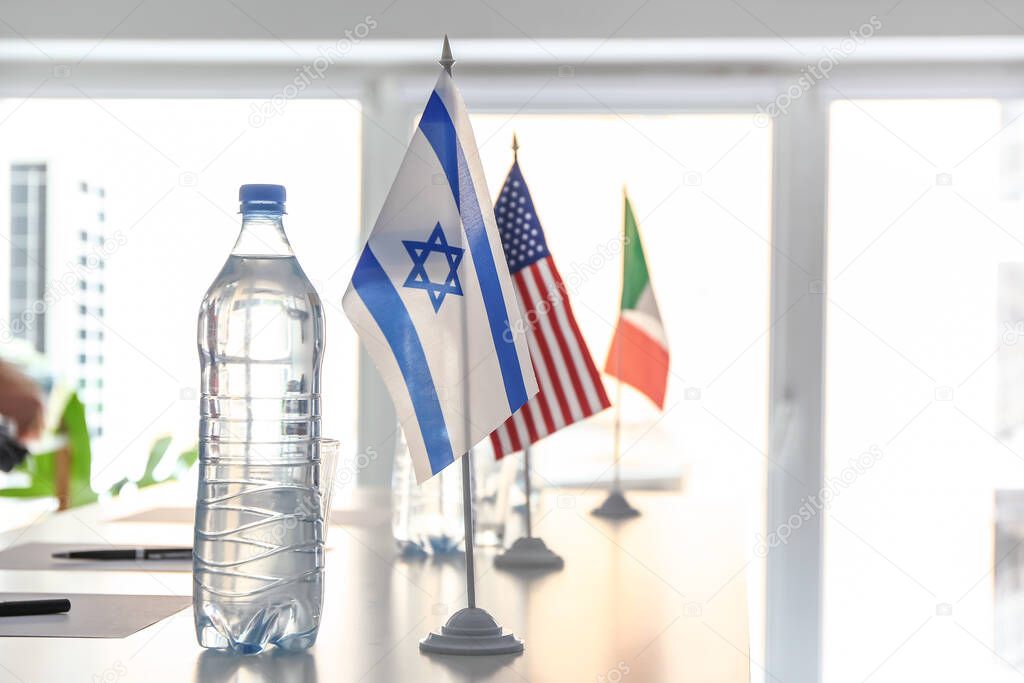 Bottle with water and flags of Israel, USA and Italy on table in embassy office