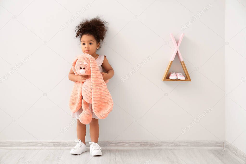 Cute African-American baby girl with toy in room