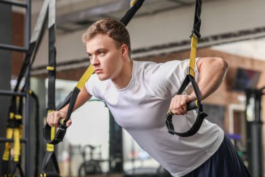 Spor salonunda TRX kayışlarıyla egzersiz yapan yakışıklı kaslı adam.