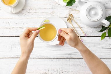 Ahşap masada yeşil çay ve limon dolu kadın elleri.