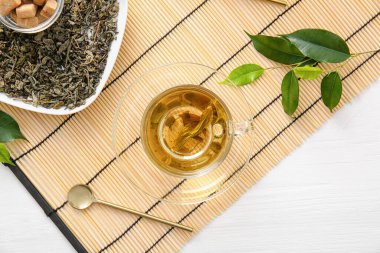 Bir fincan yeşil çay ve kuru yapraklı bambu paspası.