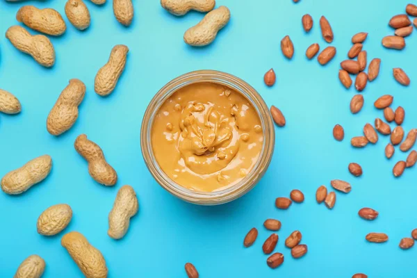 Jar with tasty peanut butter and nuts on color background