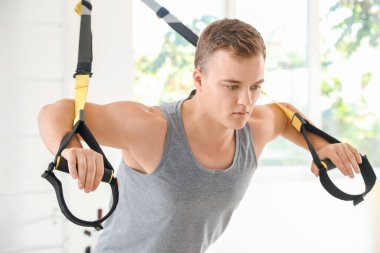 Spor salonunda TRX kayışlarıyla spor yapan genç adam.