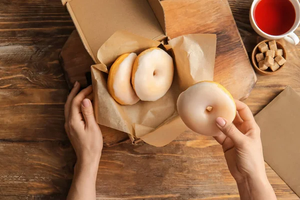 Ahşap arka planda lezzetli donutları olan kadın elleri.