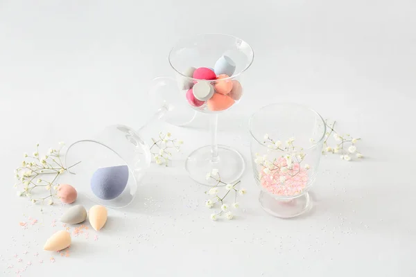 Glasses with makeup sponges on light background