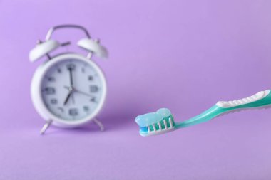Yapıştırıcılı diş fırçası ve renk arkaplanındaki alarm saati