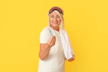 Uyku maskeli olgun bir kadın ve arka planda diş fırçası var.