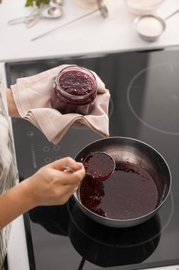 Kadın mutfakta ahududu reçeli pişiriyor.