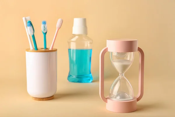 Toothbrushes, mouth rinse and hourglass on light background