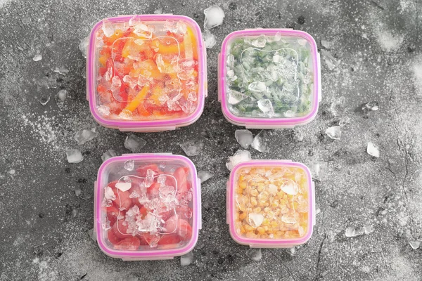 深色背景下装有冷冻蔬菜和冰块的塑料容器 — 图库照片