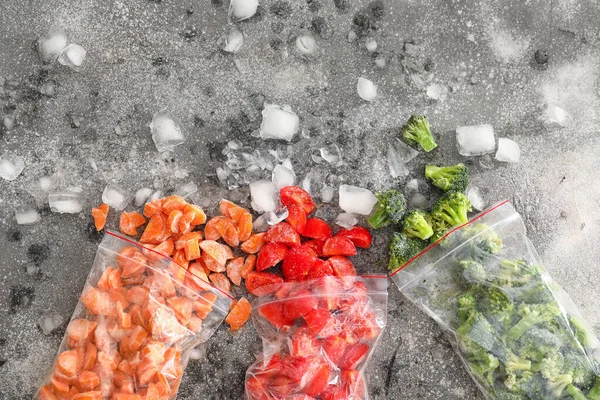 Plastic bags with frozen vegetables and ice on dark background