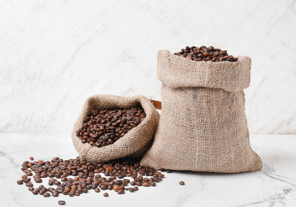 Bags with coffee beans on light background