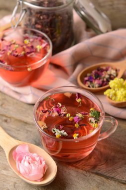 Bir fincan çiçekli çay ve tahta arka planda kuru çiçekli kaşıklar.
