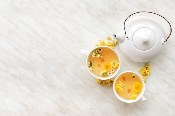 Teapot and cups with floral tea on light background