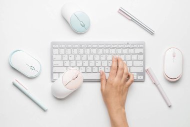 Beyaz arkaplanda bilgisayar klavyesi ve faresi olan kadın eli
