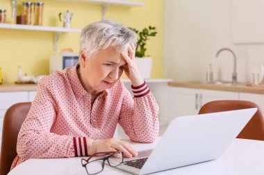 Evde baş ağrısı çeken stresli yaşlı kadın.