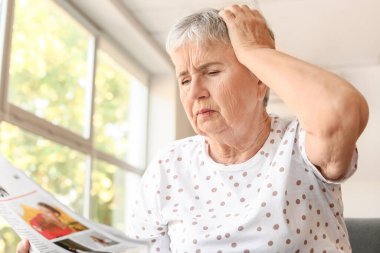 Evde gazete okuyan stresli yaşlı kadın.