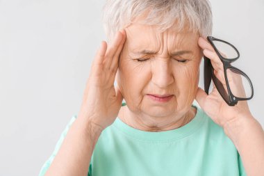 Stresli yaşlı kadın arka planda baş ağrısı çekiyor.