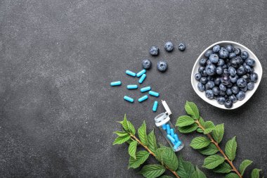 Bitki bazlı haplar ve koyu arkaplanda yabanmersinli kase.