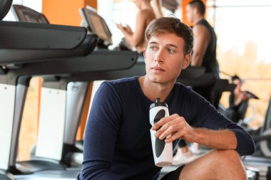 Koşu bandında antrenmandan sonra su içen genç adam.