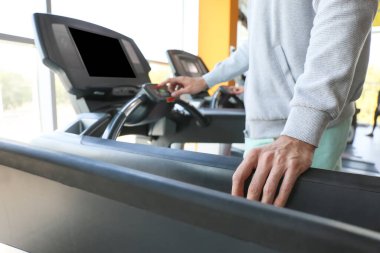 Spor salonundaki koşu bandında antrenman yapan genç adam, yakın plan.