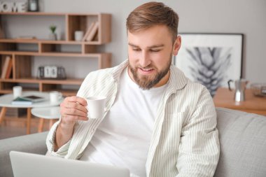 Laptoplu genç adam evde sıcak kahve içiyor.