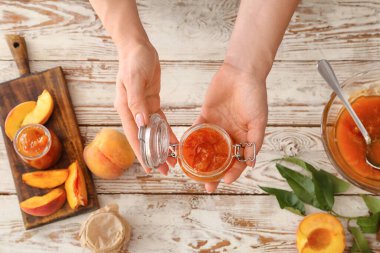 Ahşap arka planda lezzetli şeftali reçeli kavanozu olan kadın elleri.